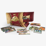 Jurassic Park X-Dominion Park collectible card set displayed with its red and gold presentation box, a smaller inner box, and several scattered cards showing dinosaur and character illustrations on a light gray background.