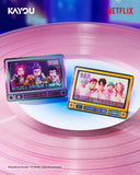 Two rectangular pin-style accessories displayed on a pink vinyl record background. Each pin features colorful cartoon and group-photo graphics with text including SSR, HUNTRx, and SOR.